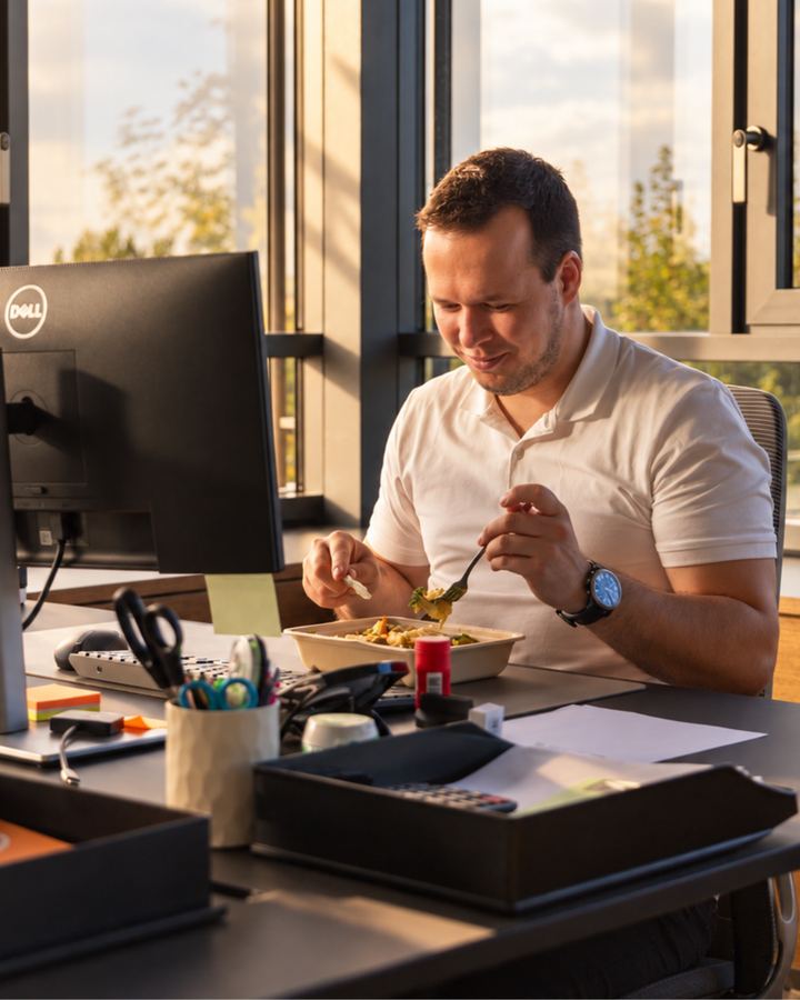 Mitarbeiter isst ein Mr.-Lunch-Gericht am Schreibtisch im Büro
